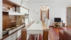 A modern dining area with a long table, white chairs, a wooden cabinet with glassware, and a television on a stand. - Holiday Home 'Blissful Haven - Soulful Stays' with Sea View, Private Terrace and Wi-Fi (Porto Moniz)