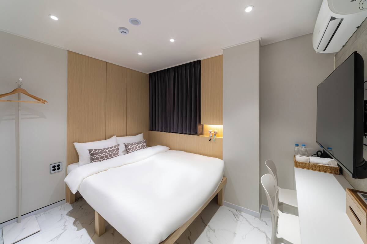 A modern hotel room with a large bed, a desk, a chair, and a television.