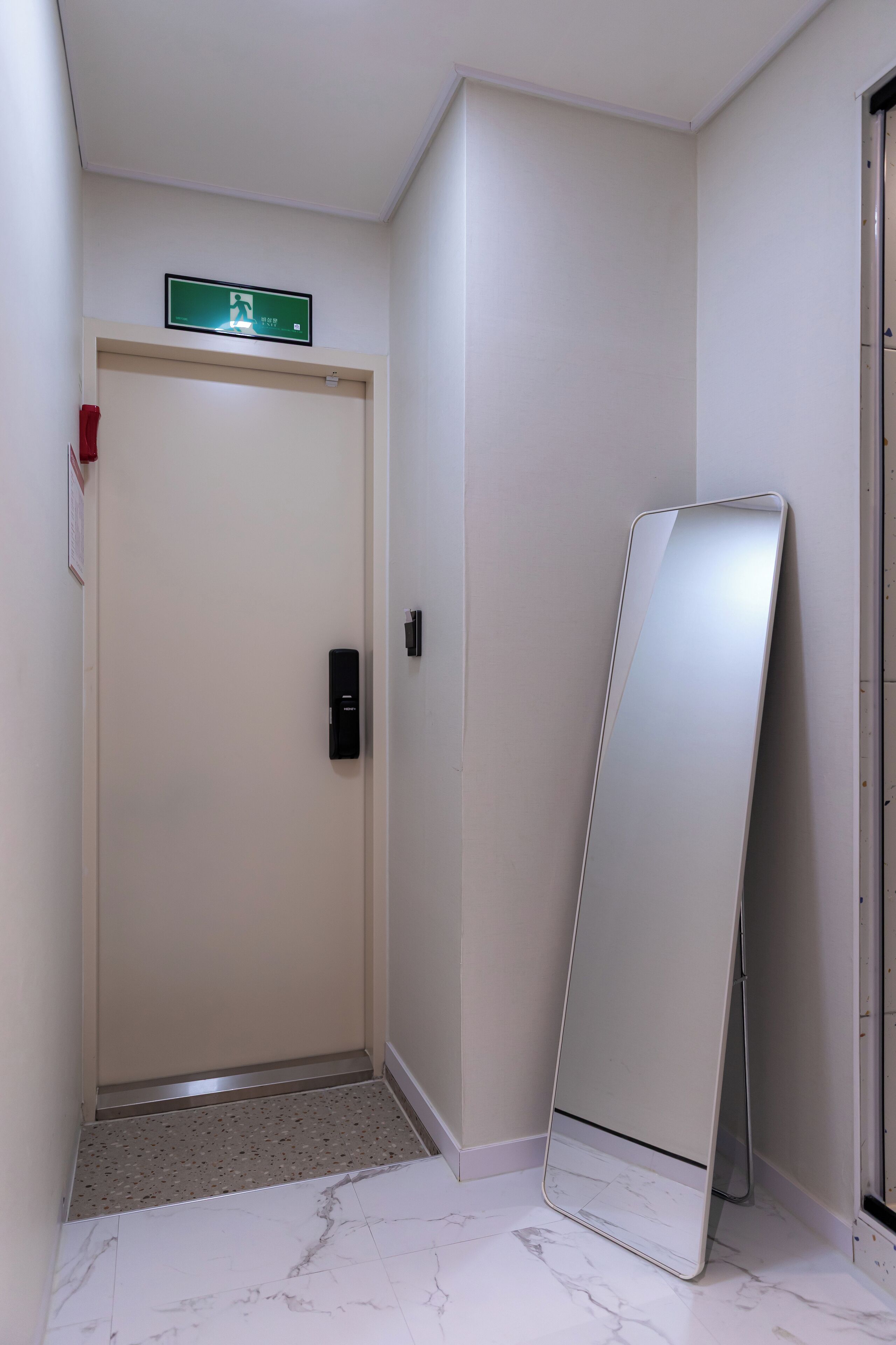 A hallway with a door, a digital sign, and a standing mirror.