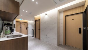 Un hall d’hôtel moderne doté d’un espace cuisine, de lambris en bois, de murs en marbre et d’un panneau de commande numérique pour l’ascenseur.