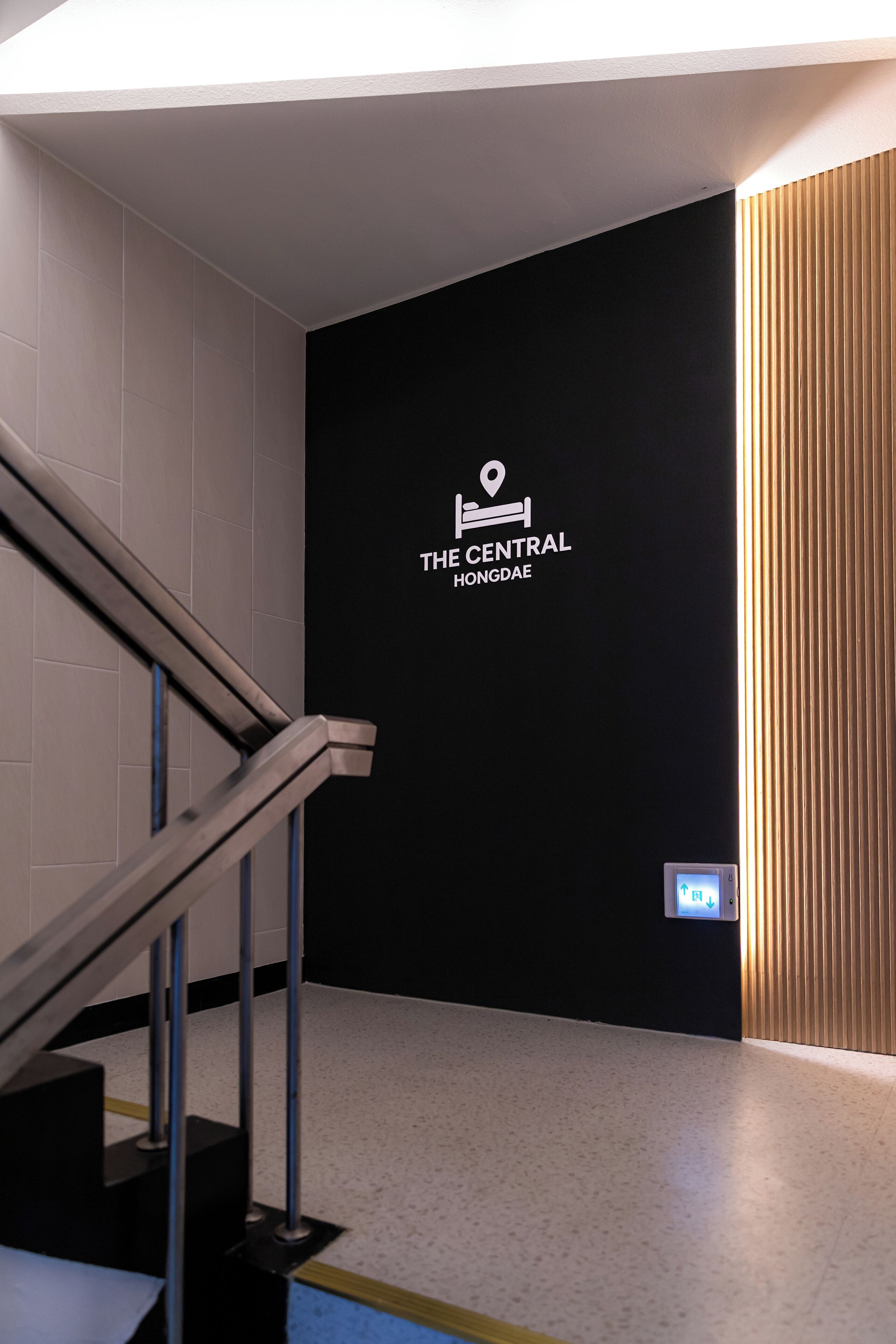 Una escalera lleva a una pared negra con un logotipo y texto que indica 'THE CENTRAL HONGDAE'.