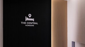 Un couloir avec un mur noir orné d’un logo et du nom « The Central Hongdae ».