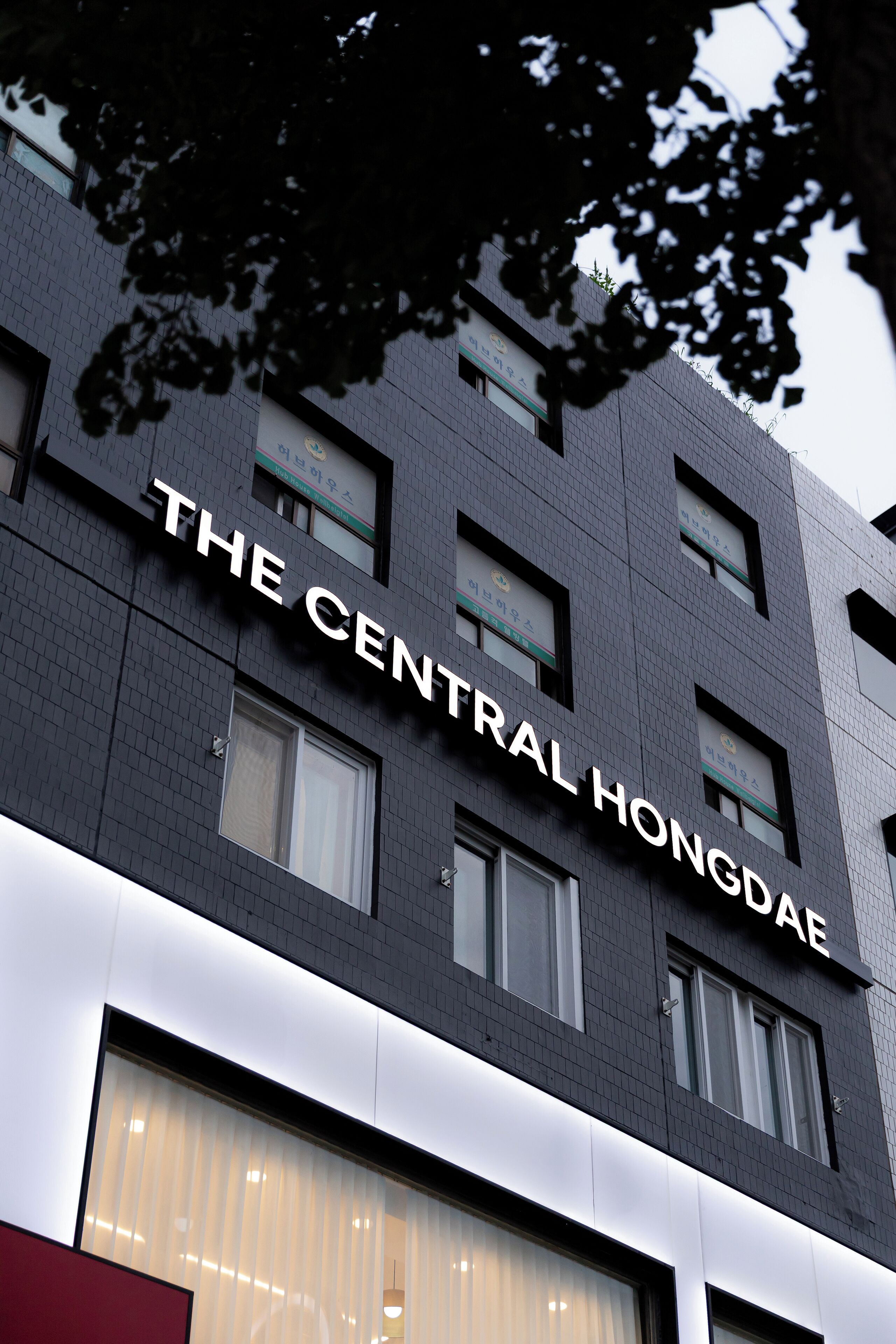 A building with "THE CENTRAL HONGDAE" signage, featuring a modern architectural style with multiple windows and a brick facade.