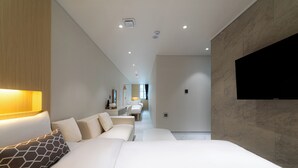 Une chambre d’hôtel moderne avec un grand lit, un téléviseur fixé au mur et un couloir menant à la salle de bain.