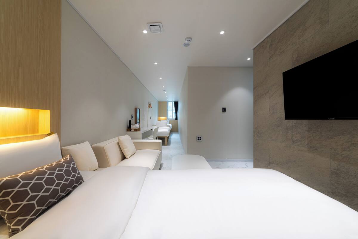 A modern hotel room with a large bed, a TV mounted on the wall, and a hallway leading to a bathroom.