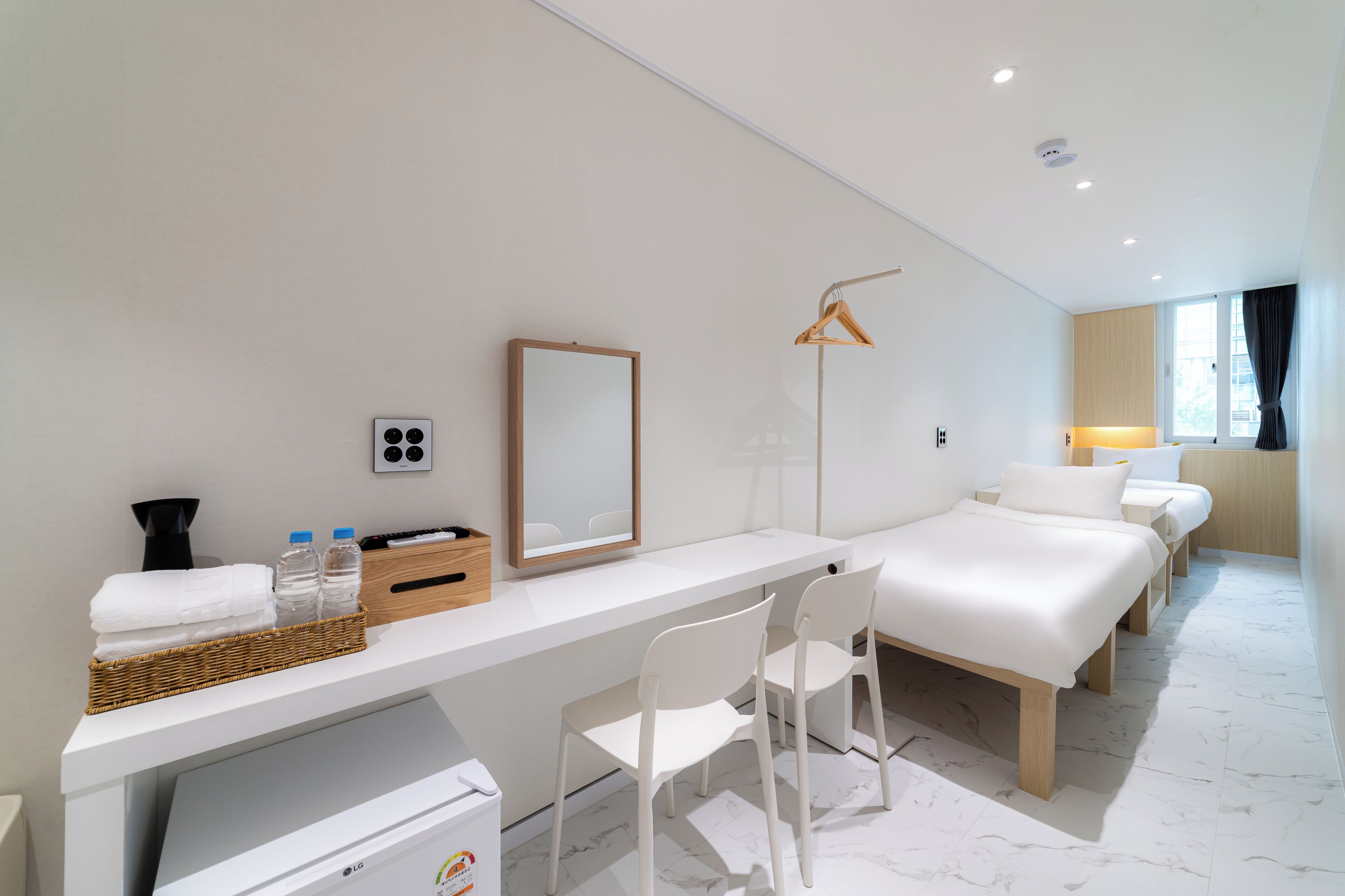 A hotel room with a bed, a desk, a chair, a mirror, a lamp, and a window with curtains.
