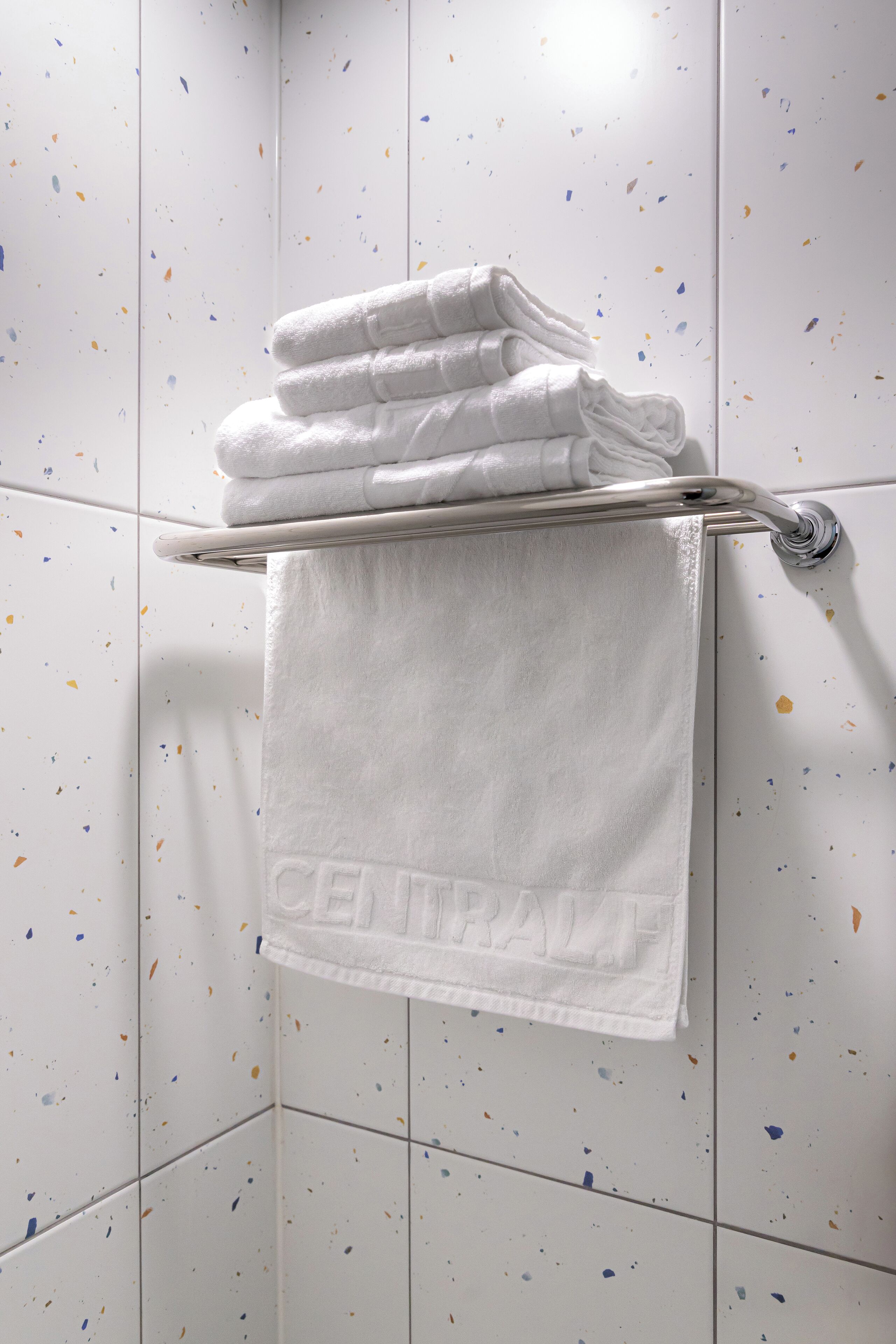 A bathroom with white speckled tiles and a towel rack holding folded white towels.