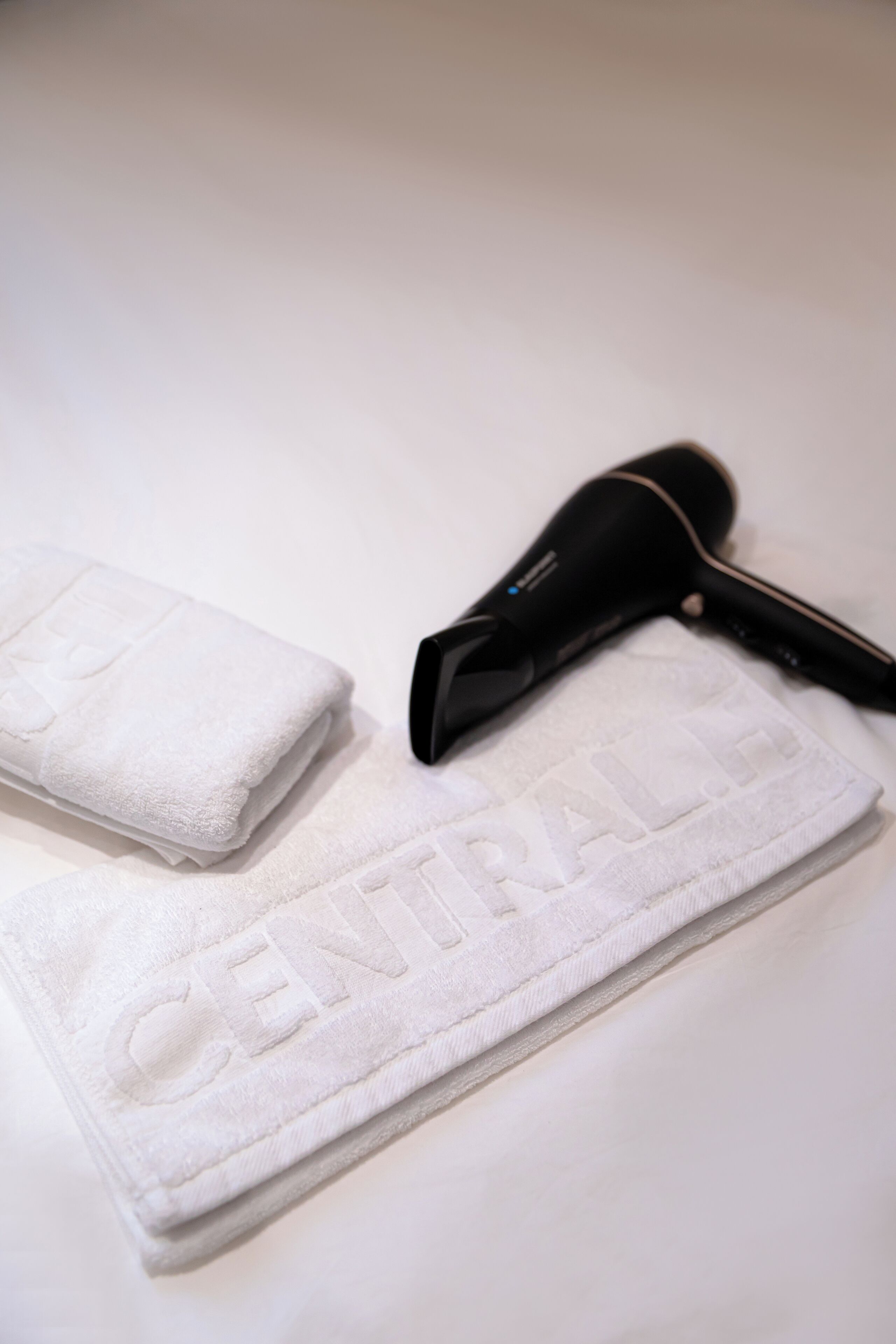 A white towel with the word "CENTRAL" embossed on it and a black hair dryer on a white surface.