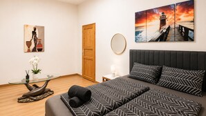 A hotel room with a bed, a glass table with a vase of flowers, a painting of a woman and vases, a wooden door, and a large painting of a lighthouse. - Inviting Getaway Near FAC Platz (Vienna)