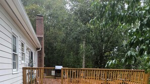 Una terraza de madera que conduce a una casa con una chimenea de ladrillo, rodeada de árboles.