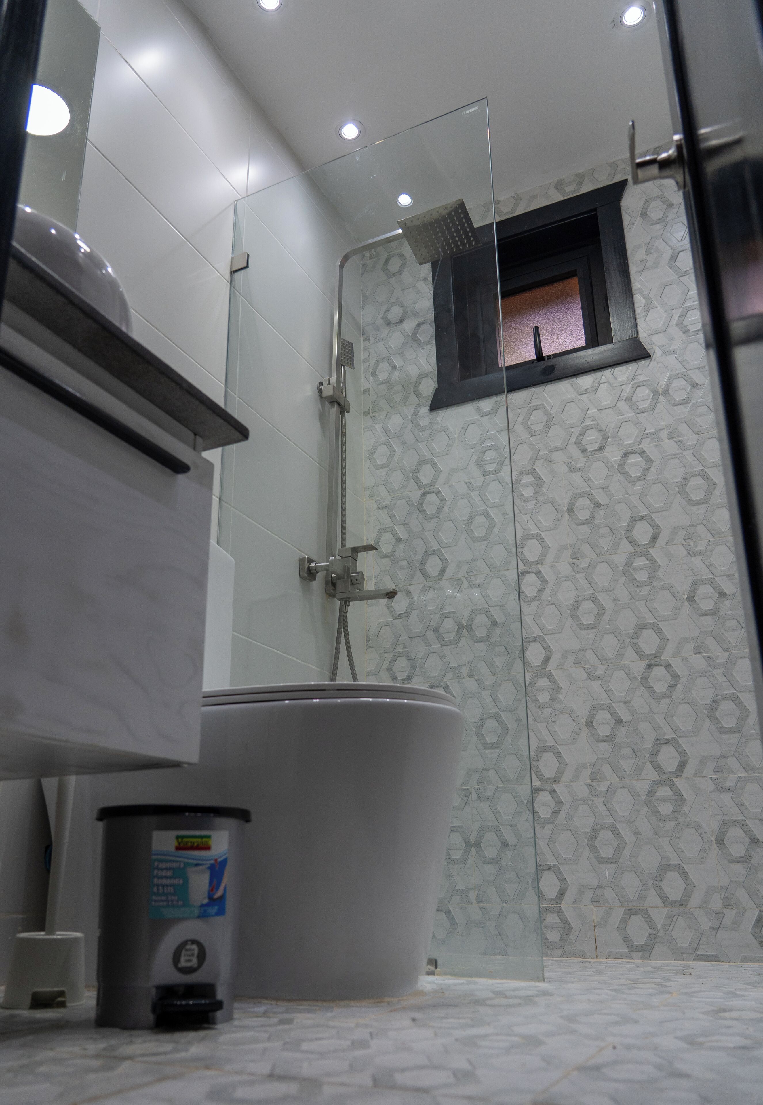 Een badkamer met toilet, een prullenbak en een douche met glazen deur.