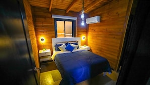 A compact wooden room with a bed, bedside tables, and a window. - Villa Dulce Refugio (Cabrera)