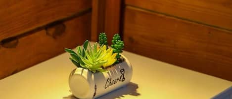 Uma pequena mesa branca com uma planta em vaso e um candeeiro fixado na parede.