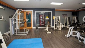 A gym with various exercise machines, a blue mat, and a door leading to another room.