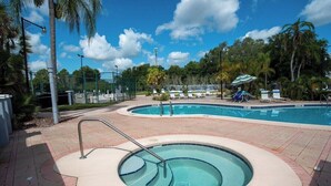 A swimming pool with a small hot tub, surrounded by palm trees and lounge chairs.