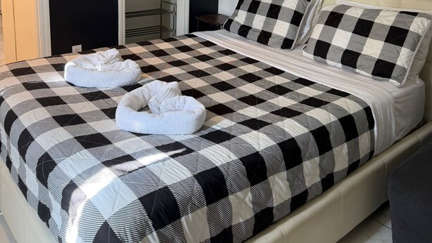 A bed with a checkered bedspread, two pillows, and two towels on the bed.