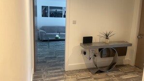 Ein modernes Wohnzimmer mit einem grauen Sofa, einem Glastisch und einem kleinen Beistelltisch mit einer Pflanze.