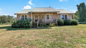 A single-story house with a porch, a front yard, and a metal roof.