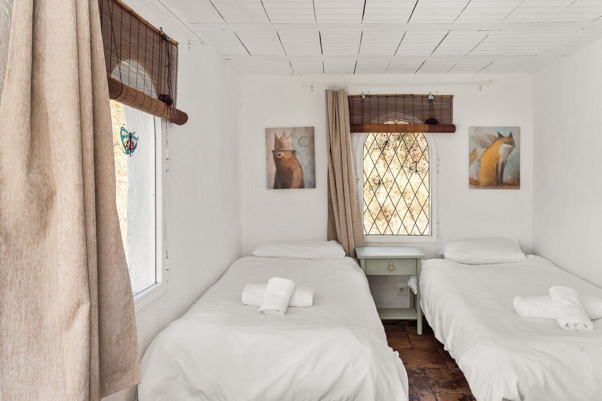 A room with two beds, a window with a view, and a painting of a fox.