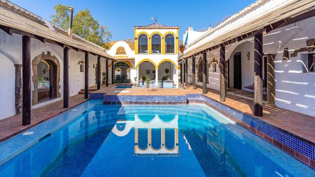 Ein Pool mit klarem, blauem Wasser, umgeben von einem Innenhof mit Bögen und einem zentralen Gebäude mit gelb-weißen Wänden.