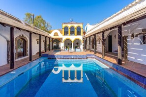A pool with a clear blue water feature, surrounded by a courtyard with arches and a central building with yellow and white walls.