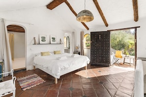 Un dormitorio con cama, lámpara colgante, ventana y puerta que da a un espacio exterior.