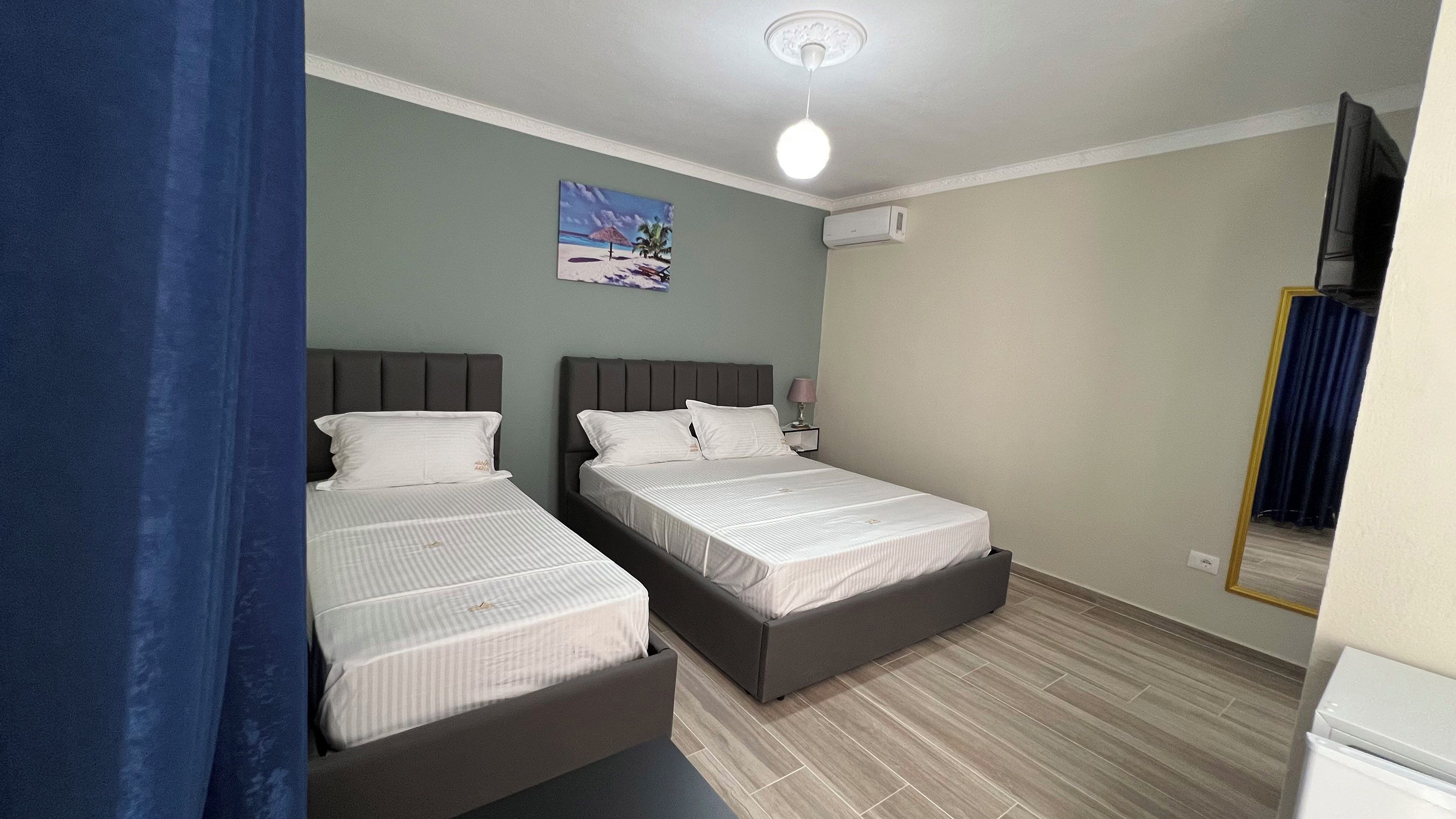 A bedroom with two beds, a ceiling fan, a painting on the wall, and a window with curtains.