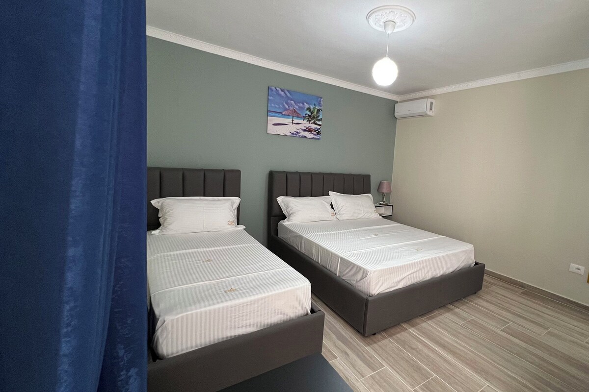 Un dormitorio con dos camas, un ventilador de techo, un cuadro en la pared y una ventana con cortinas.