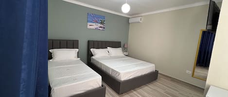 A bedroom with two beds, a ceiling fan, a painting on the wall, and a window with curtains.