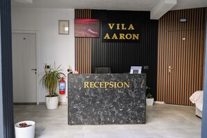 Un mostrador de recepción con una encimera de mármol y la palabra "RECEPTION" en letras doradas. Detrás, un letrero adosado a la pared dice "VILA AARON".