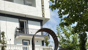 A modern hotel with a white facade, balconies, and a circular metal sculpture in the foreground. - Hotel Vila Aaron (Manëz)
