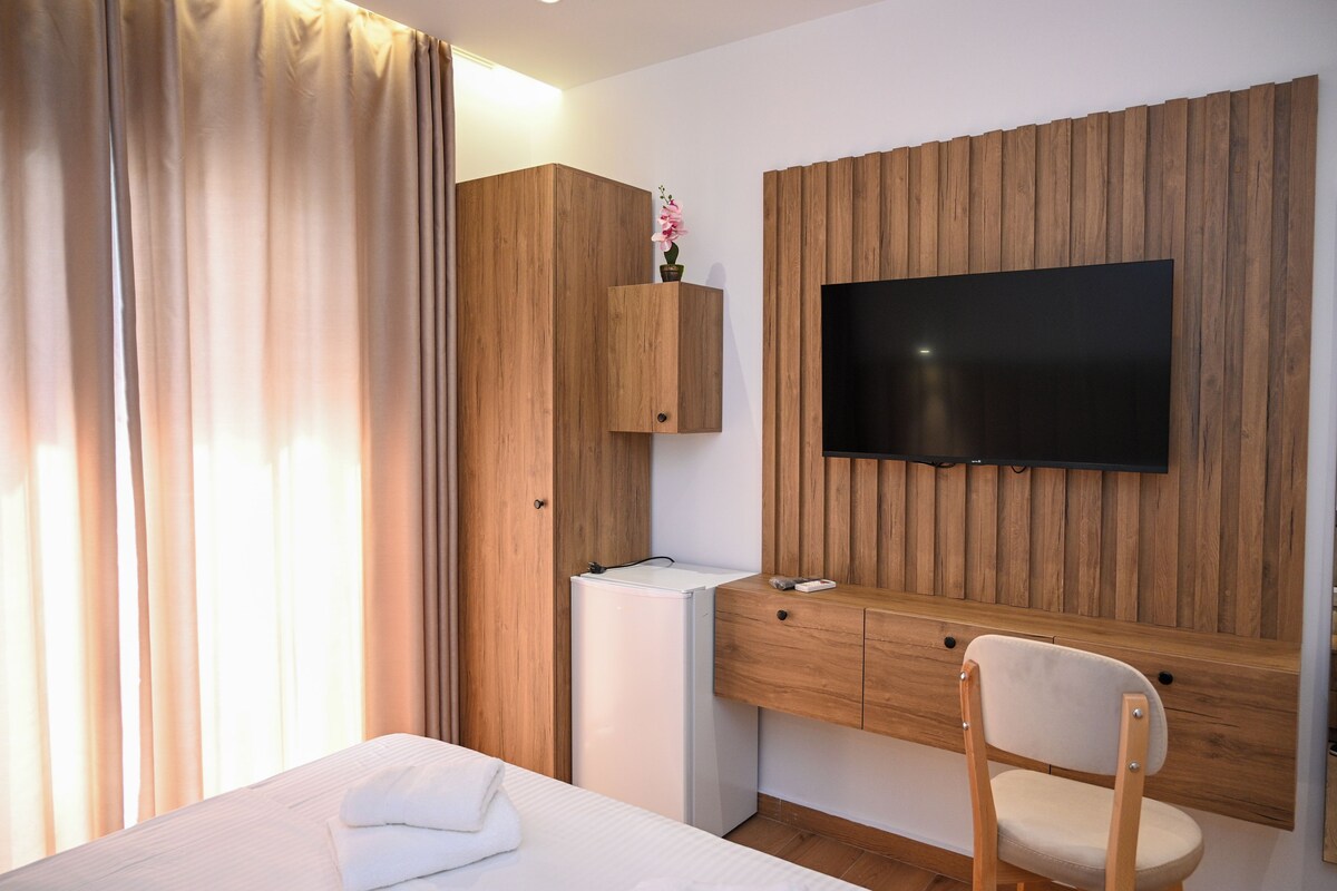 Habitación de hotel con una cama, un escritorio de madera, televisor, refrigerador pequeño y armario de madera.