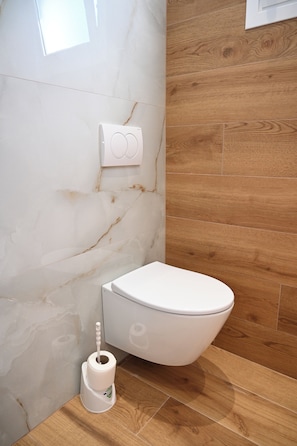 A modern bathroom with a white toilet, a marble wall, and wooden flooring. - Hotel Vila Aaron (Durrës)