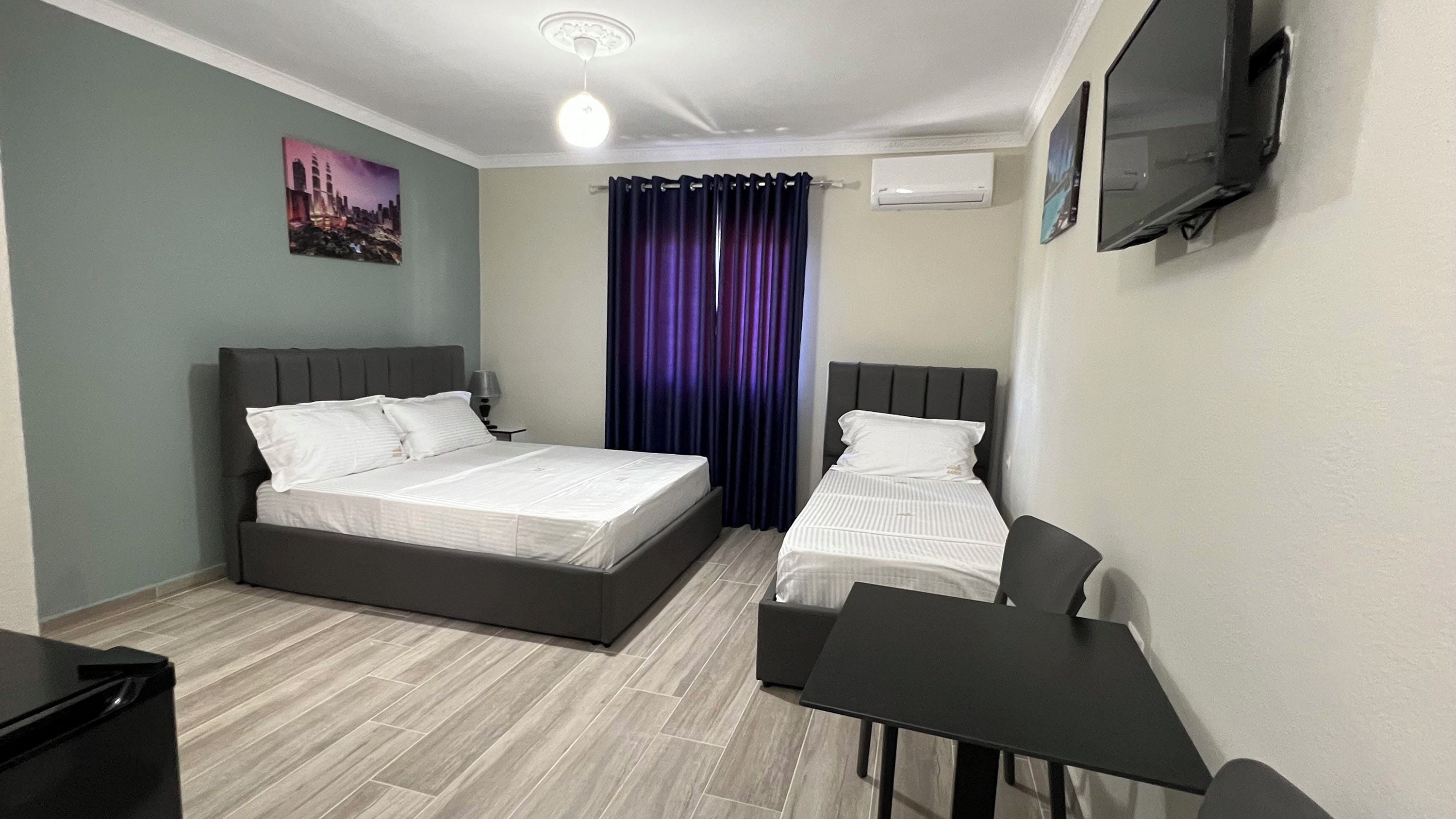 A hotel room with a bed, a desk, a chair, a TV, and a window with curtains.