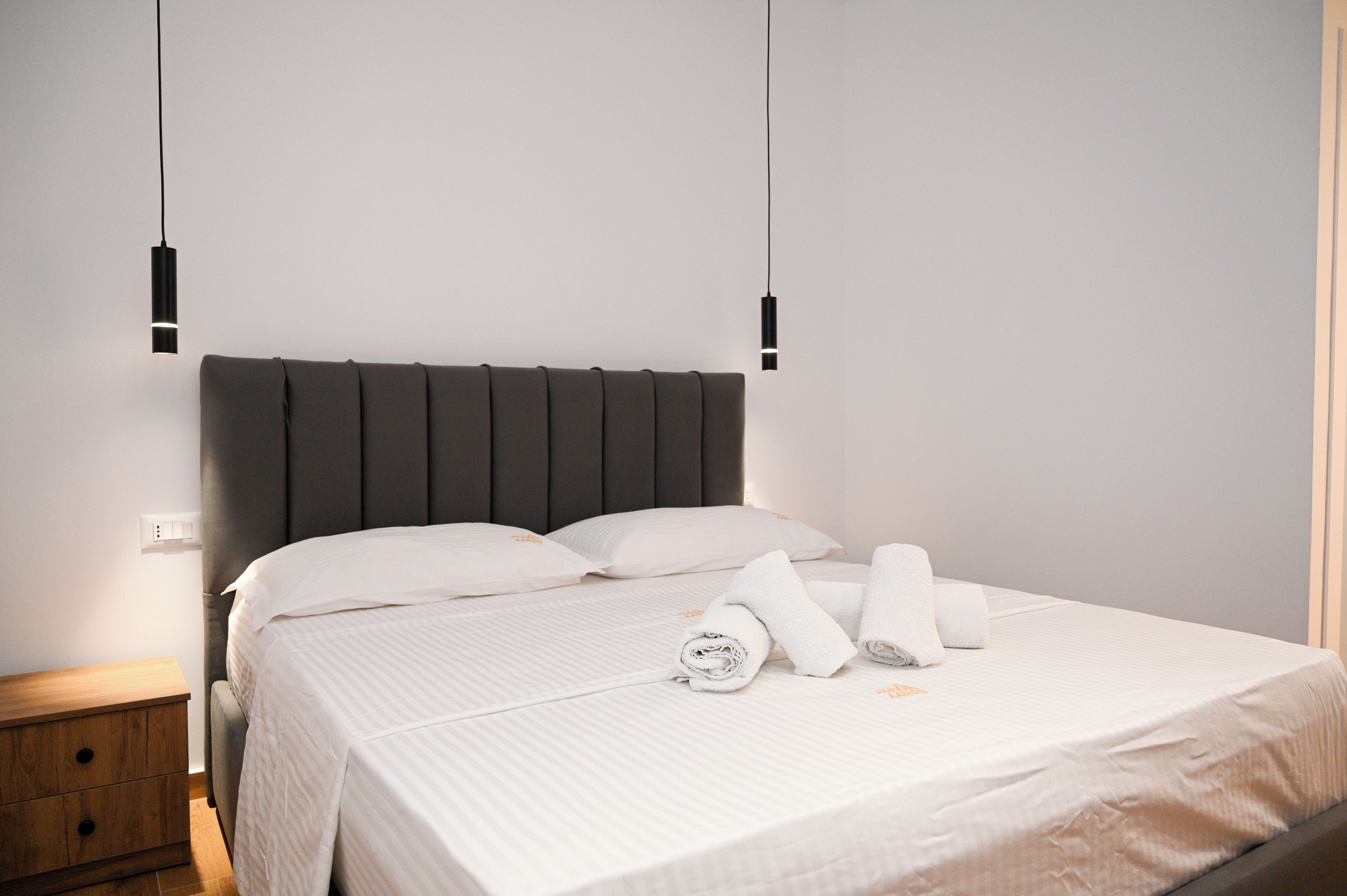 Una cama bien hecha con sábanas blancas, un cabecero oscuro y dos lámparas de noche.