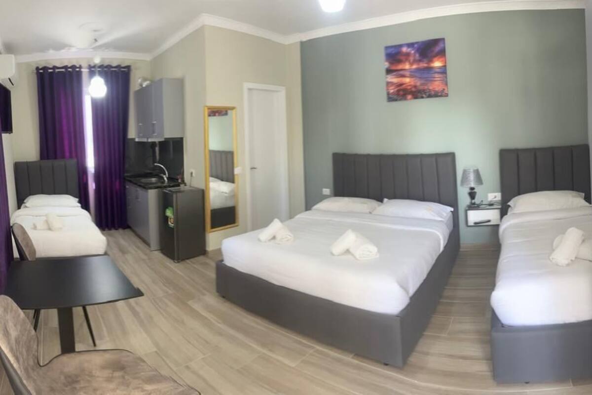 A hotel room with two beds, a desk, a chair, a small kitchenette, and a bathroom.