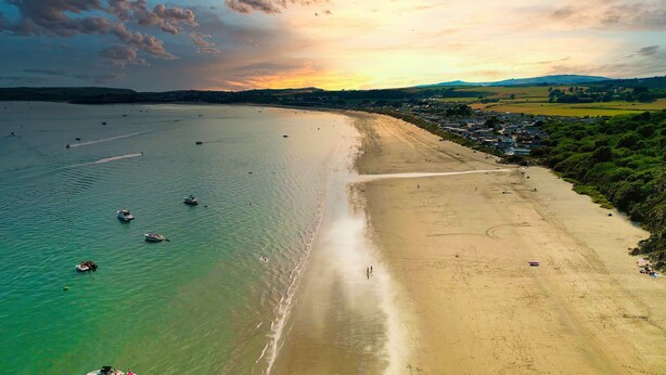Vista aérea de una playa con barcos, una orilla arenosa y un pueblo al fondo.