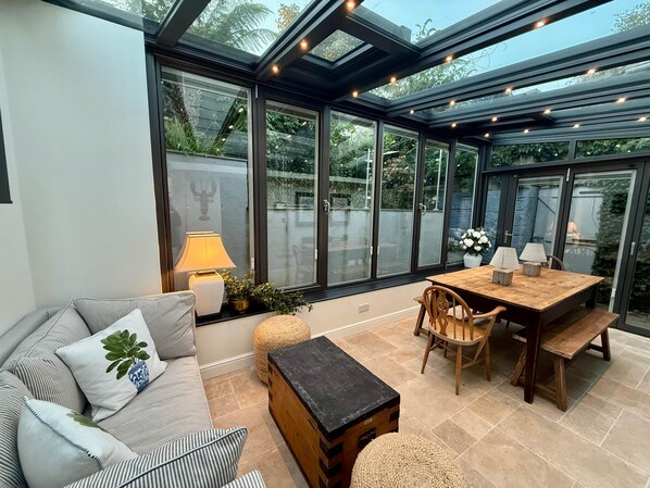 A sunlit patio with a sofa, table, chairs, and a lamp.