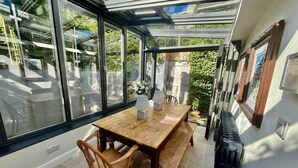 Un invernadero con una mesa y sillas de madera, amplias ventanas de vidrio y un radiador.