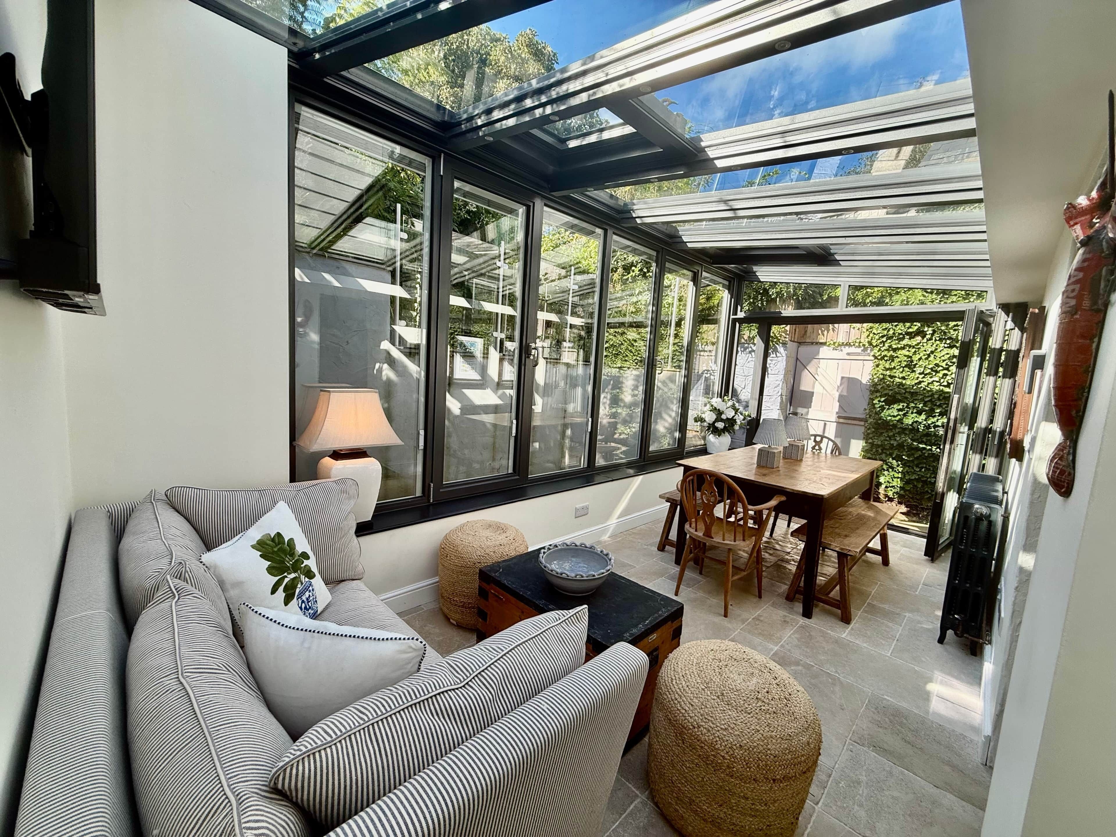 Una habitación iluminada por el sol con techo de vidrio, un sofá, una mesa y sillas.