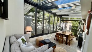 Una habitación iluminada por el sol con techo de vidrio, un sofá, una mesa y sillas.