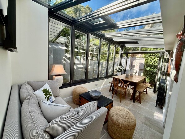 Una habitación iluminada por el sol con techo de vidrio, un sofá, una mesa y sillas.