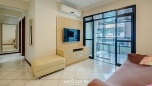 A modern living room with a flat-screen TV, a sofa, and a sliding glass door leading to a balcony. - Apt w Balcony nd Barbecue in Seaside Condom Uar301 (Itapema)