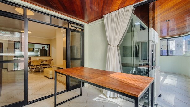 A modern interior with a wooden ceiling, a glass sliding door, a wooden table, and a view of a kitchen and dining area. - Apt w Balcony nd Barbecue in Seaside Condom Uar301 (Itapema)