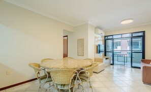 A dining area with a round table and wicker chairs, a sofa, and a large window with a view.