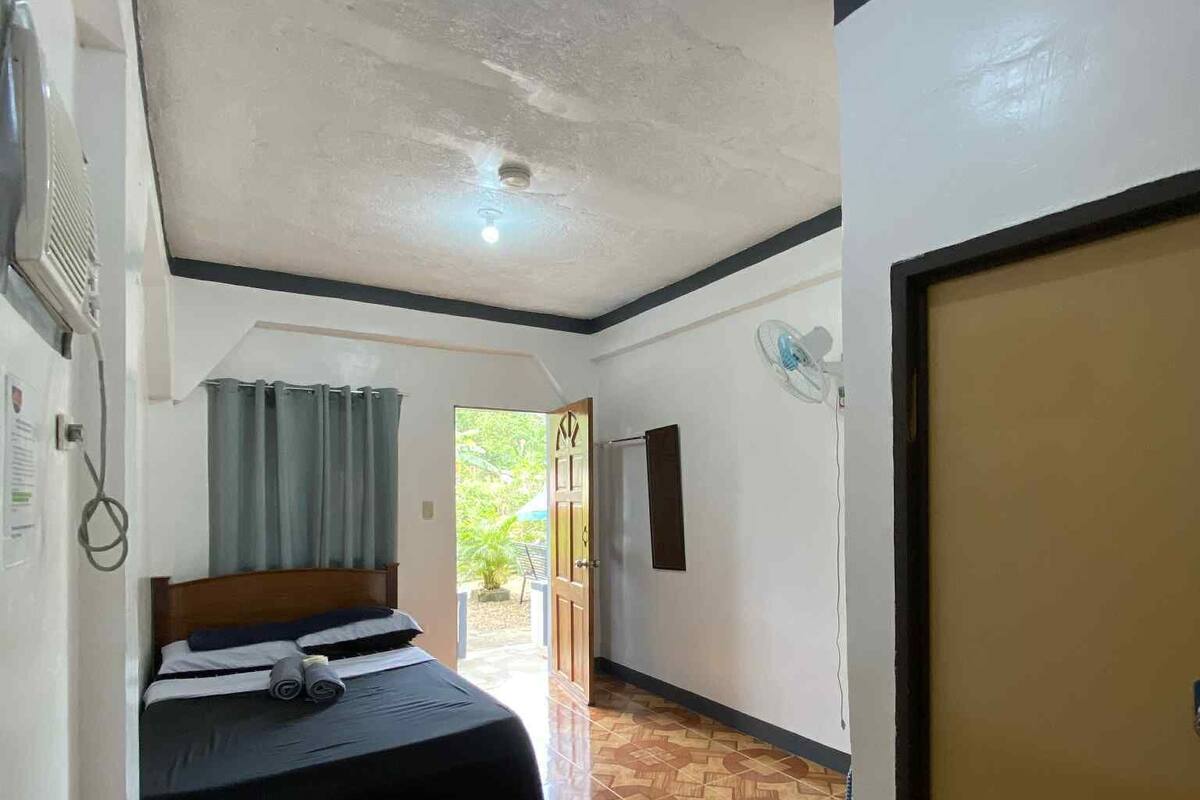 A hotel room with a bed, a ceiling fan, a door, and a patterned floor.