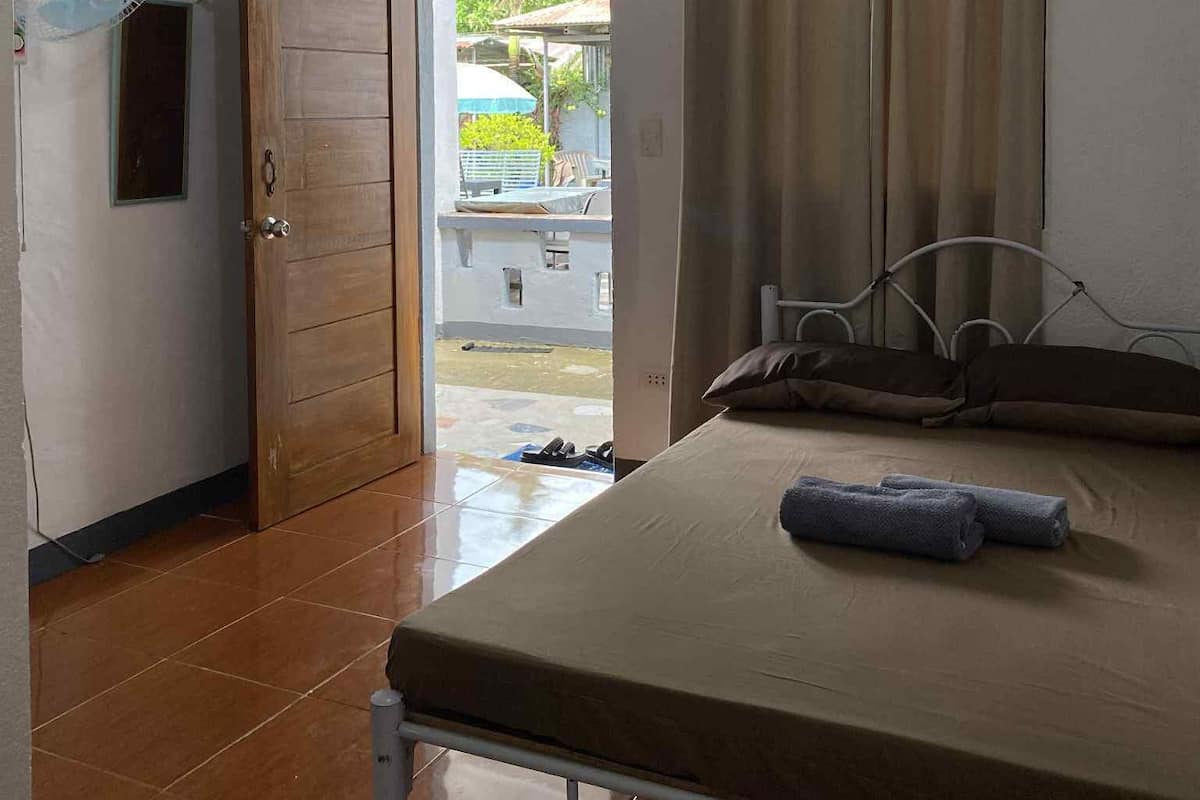 A room with a bed, a fan, a door, and a view of the outside.