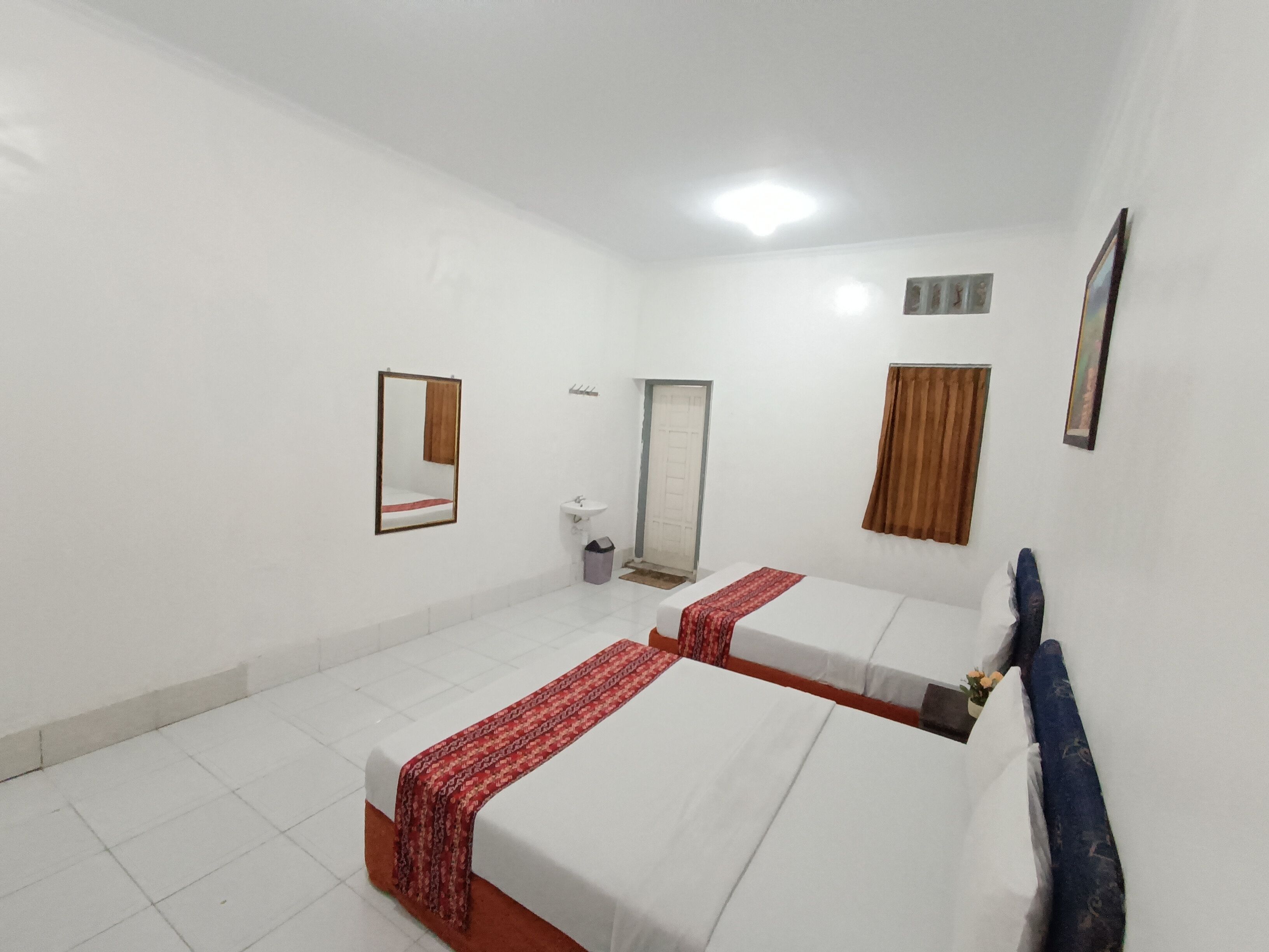 A hotel room with two single beds, a small bathroom, and a white tiled floor.