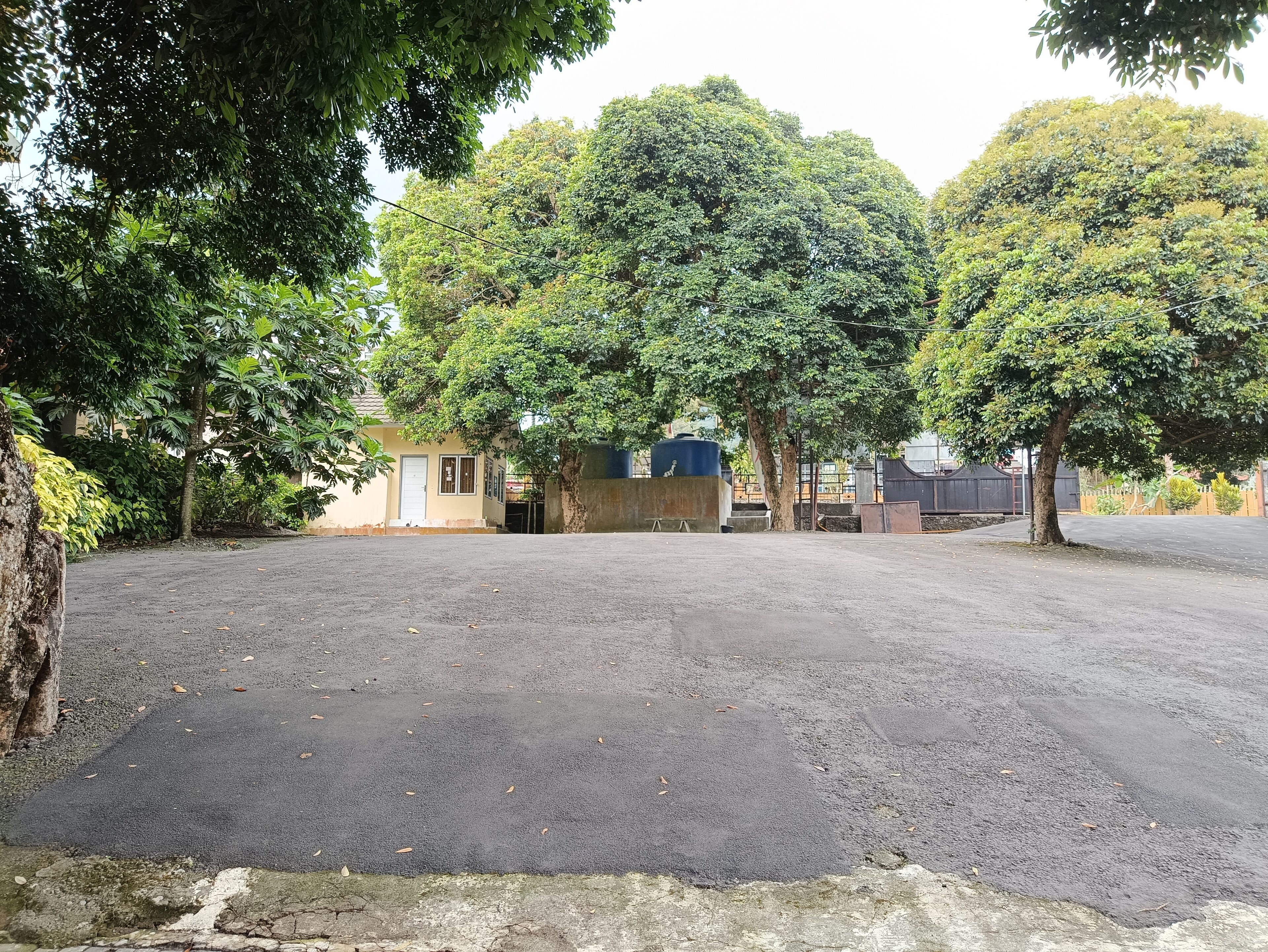 A paved parking area with trees and a small building.