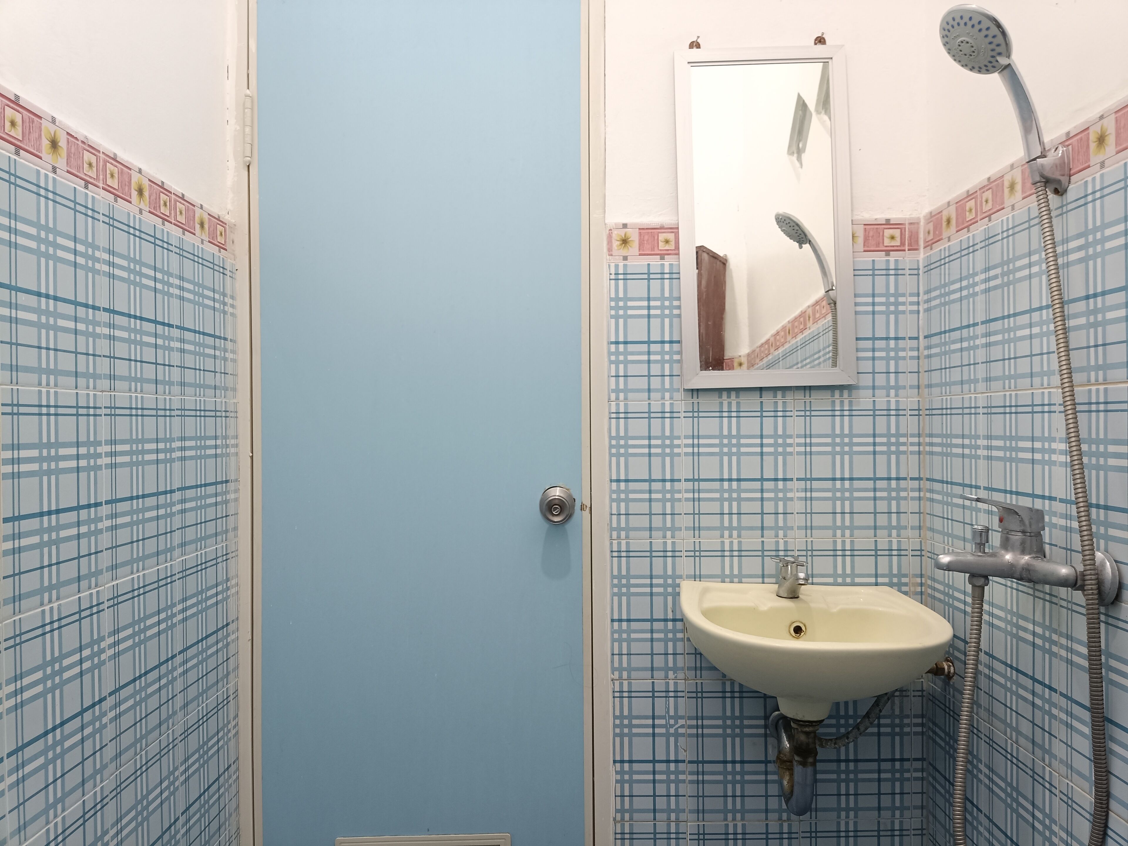 A bathroom with blue checkered tiles, a white sink, a handheld showerhead, and a mirror on the wall.